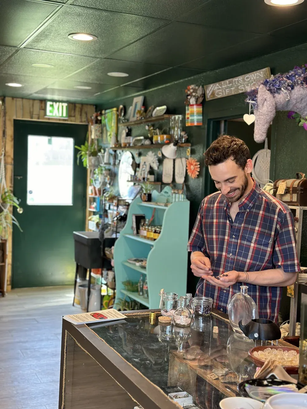 At the All Its Own gift shop counter, surrounded by plants and local makers' work